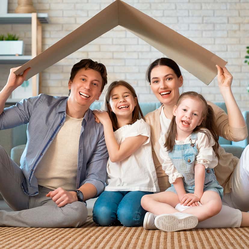 Una famiglia, due adulti e due bambine, sostengono un cartone a forma di tetto spiovente sulla loro testa